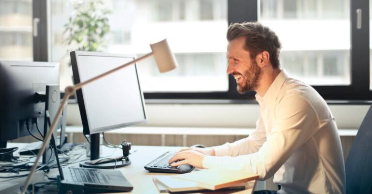 Computer - Man in White Dress Shirt Sitting on Black Rolling Chair While Facing Black Computer Set and Smiling