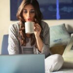 Laptop - Woman in Grey Jacket Sits on Bed Uses Grey Laptop