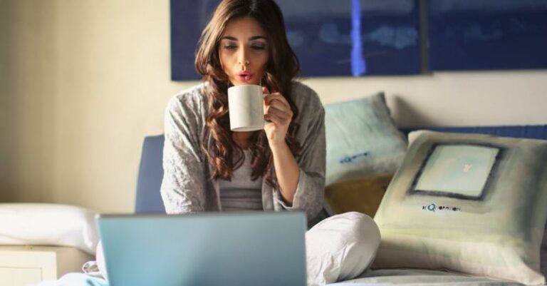 Laptop - Woman in Grey Jacket Sits on Bed Uses Grey Laptop